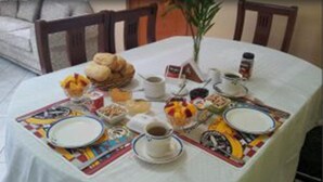 Une table de salle à manger ronde, recouverte d’une nappe blanche, mise avec des assiettes, des bols et un pichet de café.