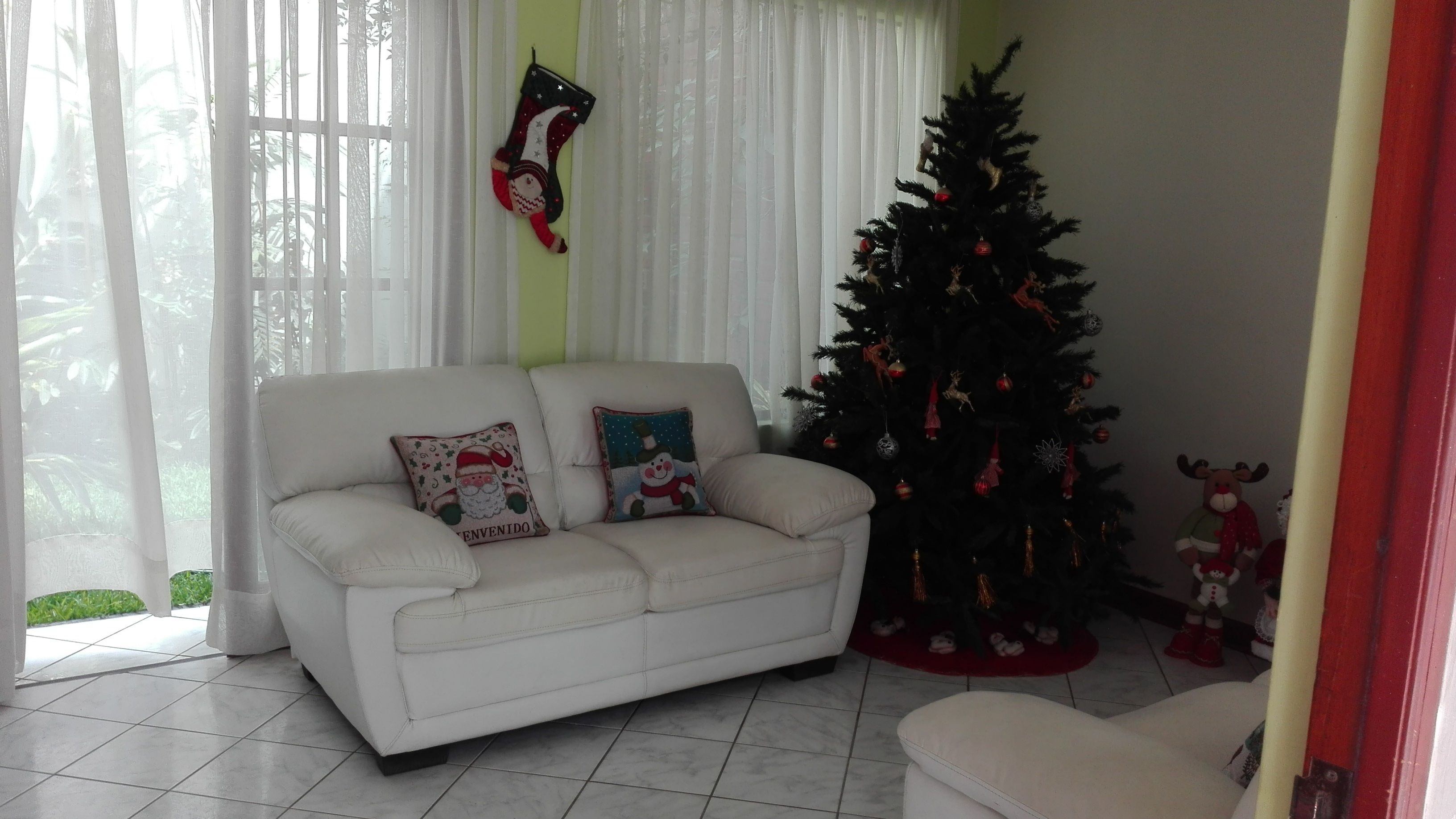 A living room with a white sofa, two decorative pillows, a Christmas tree, and a small reindeer figure.