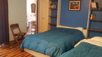 A bedroom with two beds, a wooden floor, a chair, a wardrobe, and a painting on the wall.