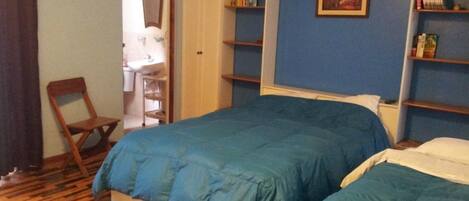 Un dormitorio con dos camas, piso de madera, una silla, un armario y un cuadro en la pared.