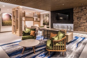 Una sala de estar moderna con sofá, sillón y mesa de centro. Hay una chimenea con azulejos decorativos y un televisor montado en la pared.