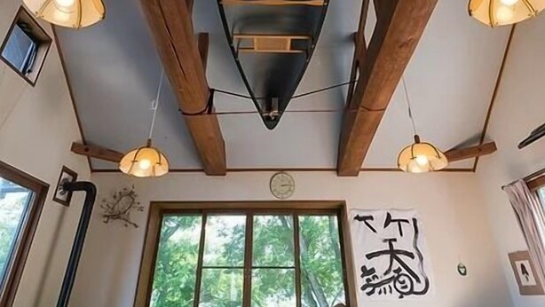 Un interior acogedor con vigas de madera, un sofá verde, una zona de comedor con sillas y un televisor.