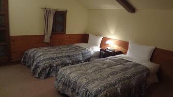 A room with two beds, a window with curtains, a nightstand with a lamp, and wooden beams on the ceiling.