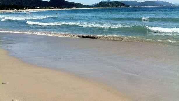A beach with clear skies, gentle waves, and distant hills. - Casa a 50 metros da praia da Armação (Florianópolis)