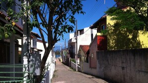A narrow street lined with residential buildings, a tree in the foreground, and utility poles. - Casa a 50 metros da praia da Armação (Florianópolis)