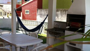 An outdoor patio with a table and chairs, a hammock, and a barbecue grill. - Casa a 50 metros da praia da Armação (Florianópolis)