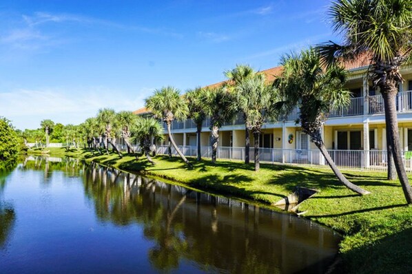 A hotel with a pool, palm trees, and a clear blue sky.