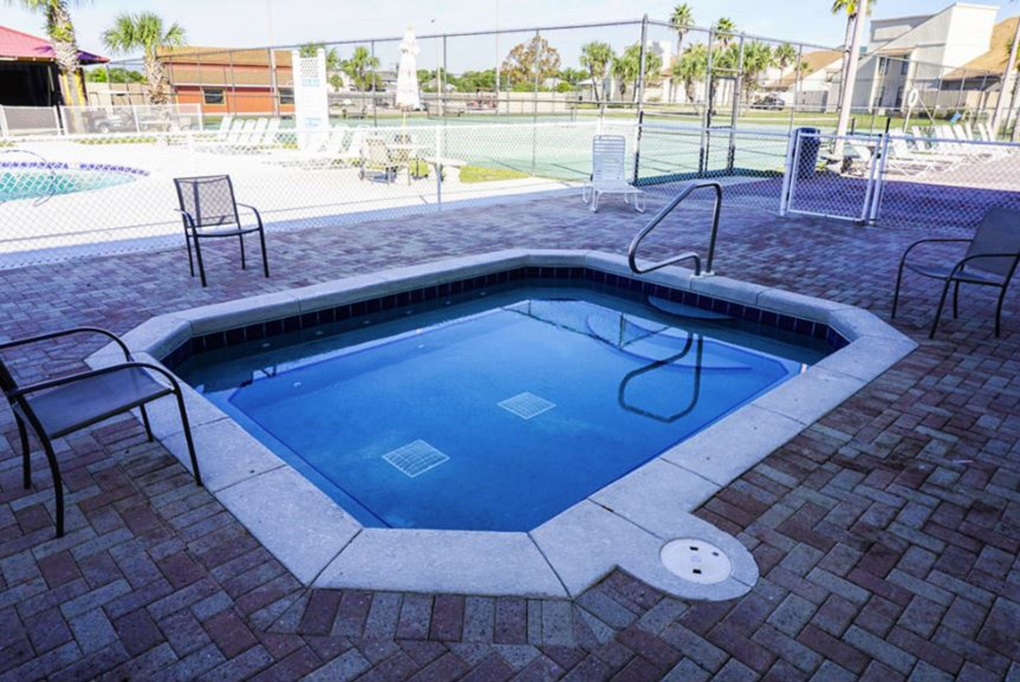 A swimming pool with a tiled edge, surrounded by brick flooring and metal chairs.