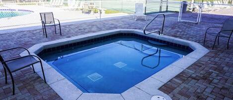 A swimming pool with a tiled edge, surrounded by brick flooring and metal chairs.