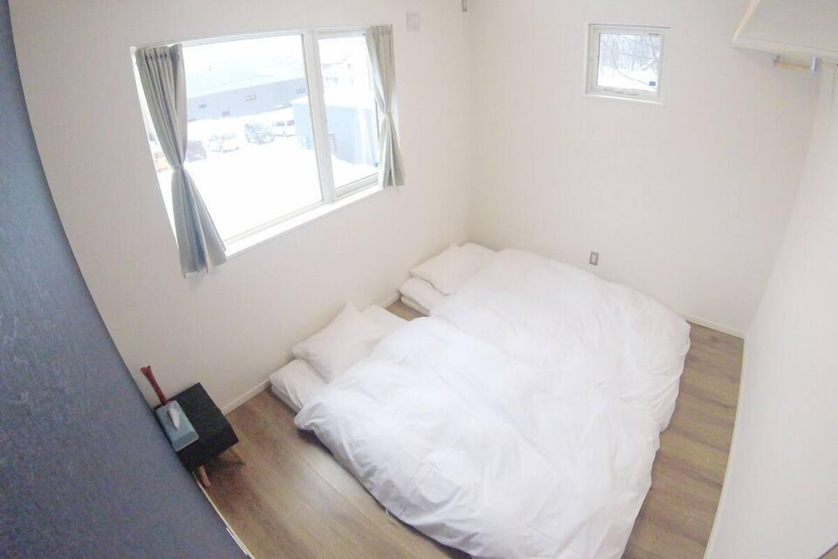 A bedroom with a large bed, two windows, and a small bedside table.