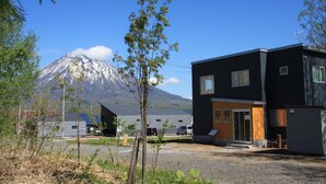 Een modern gebouw met een zwarte gevel en een gele accentmuur, gelegen in een landelijke omgeving met een berg op de achtergrond.