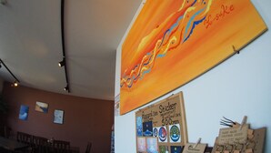Een kamer met een groot abstract schilderij aan de muur, een prikbord met stickers, en een tafel met stoelen.