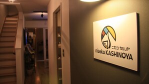 Een gang met een trap, een bordje met de tekst 'niseko KASHINOYA' en een deur naar een andere kamer.