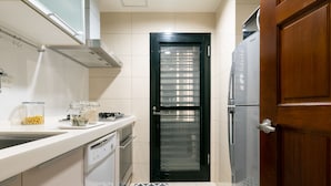 Eine kleine Küche mit weißen Schränken, einer schwarzen Tür und einem Edelstahl-Kühlschrank.