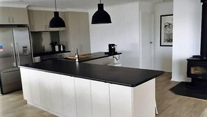 Une cuisine moderne dotée d’un îlot central, d’appareils électroménagers en acier inoxydable, de luminaires suspendus et d’une cuisinière noire.