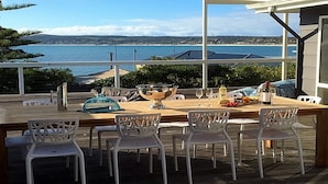 Un espace de restauration en plein air avec vue sur la mer, des tables en bois et des chaises blanches.