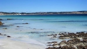 Un paysage côtier caractérisé par une eau d’un bleu limpide, une côte rocheuse et des collines qui se dessinent à l’horizon.