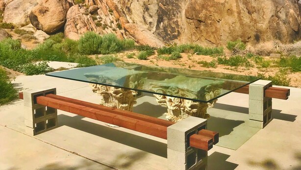 Une table à plateau de verre, entourée de bancs, le tout installé devant un décor composé de grands rochers et de montagnes.