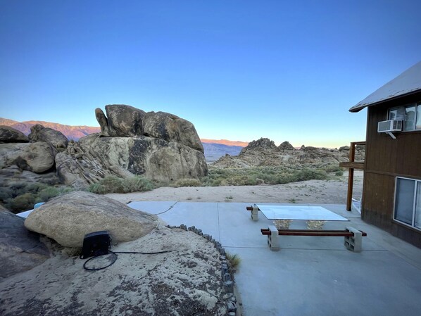 A patio area with a concrete table and a wooden bench, surrounded by large rocks and a view of mountains.