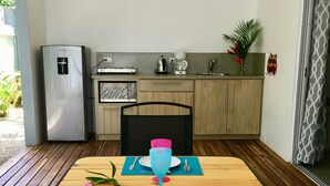 A dining area with a wooden table set for two, a chair, a water dispenser, a coffee maker, and a small plant on the counter. - El pasito is the place where you feel good at once (POTRERO)