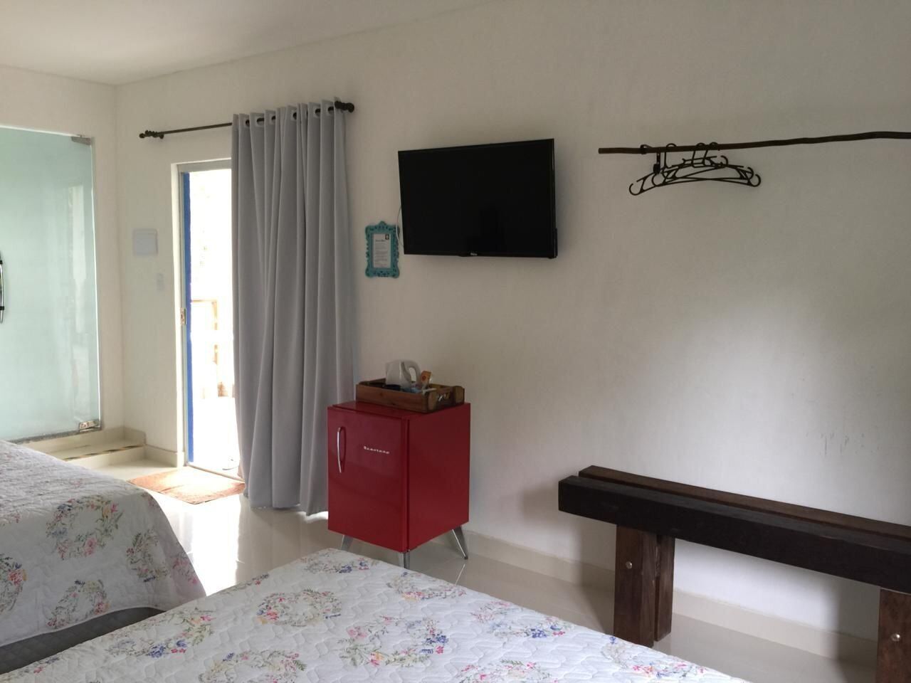 Un dormitorio con dos camas, un armario rojo, un televisor en la pared y una ventana con cortinas.