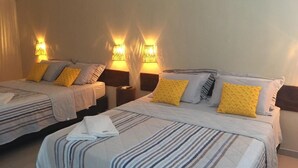 Habitación de hotel con dos camas, cada una con ropa de cama a rayas y varias almohadas. Hay lámparas fijadas a la pared que proporcionan luz.
