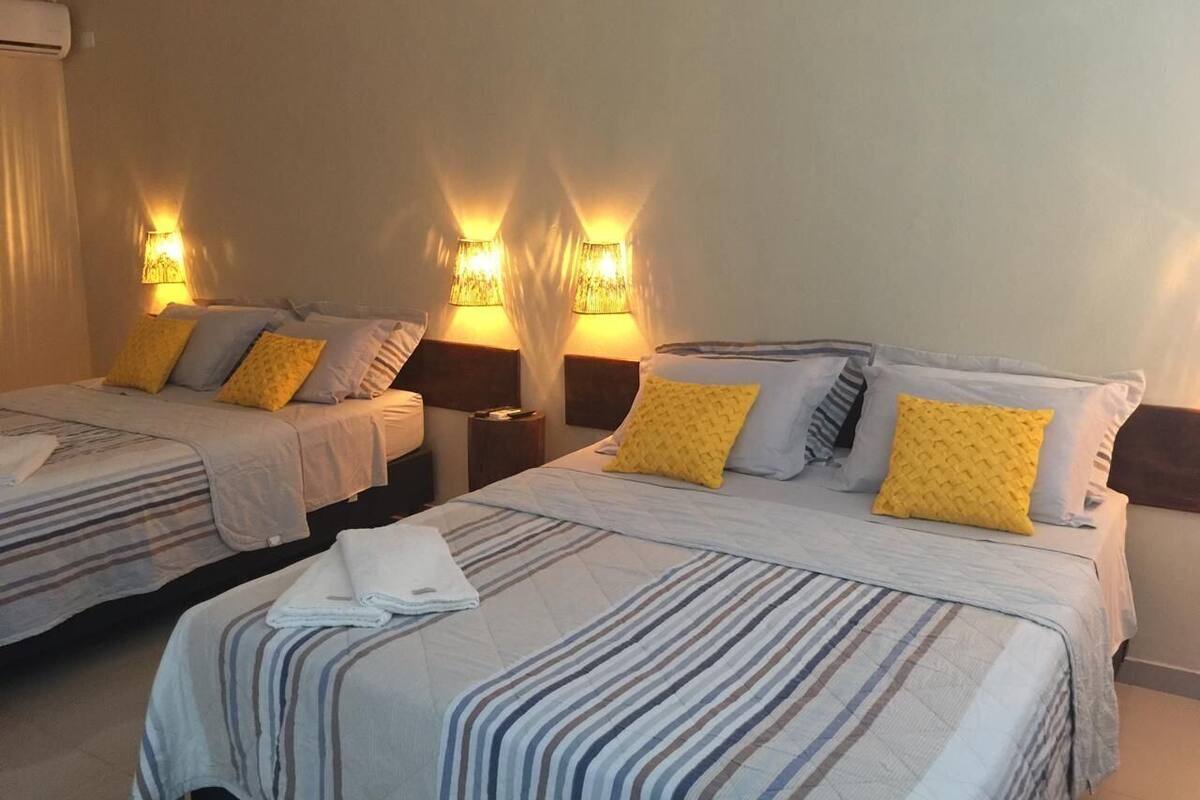 Habitación de hotel con dos camas, cada una con ropa de cama a rayas y varias almohadas. Hay lámparas fijadas a la pared que proporcionan luz.