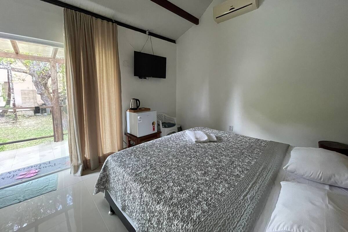 Un dormitorio con una cama, un televisor montado en la pared y una mesita con una tetera.