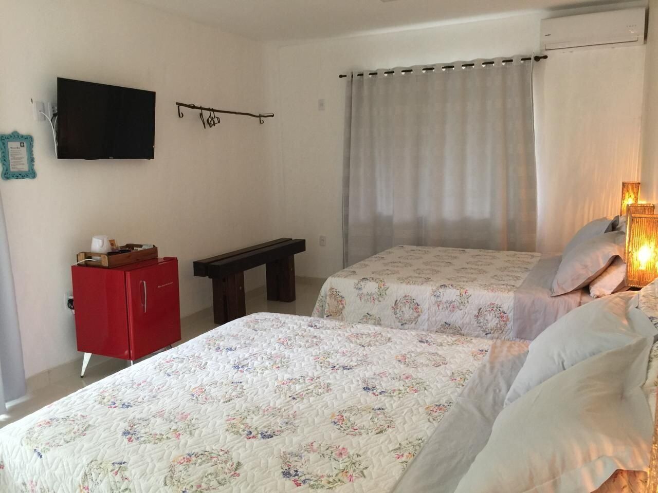 A bedroom with two beds, a red cabinet, a bench, a TV, and a curtain.