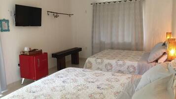 A bedroom with two beds, a red cabinet, a bench, a TV, and a curtain.