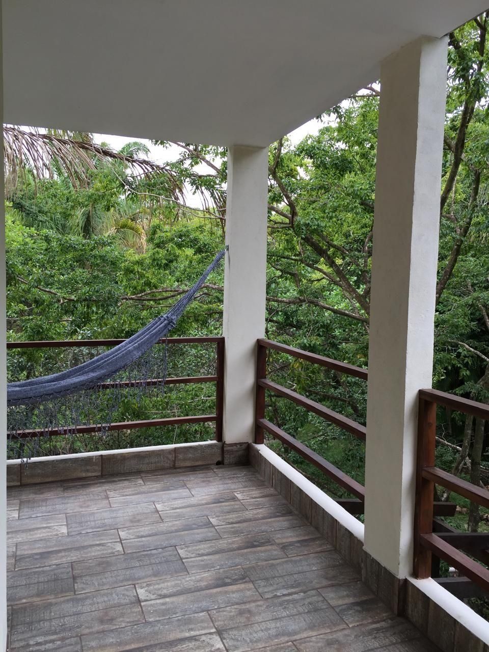 A balcony with a hammock, surrounded by lush greenery.