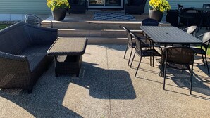 Een terras met buitenmeubilair, een schuifpui en gele bloemen.