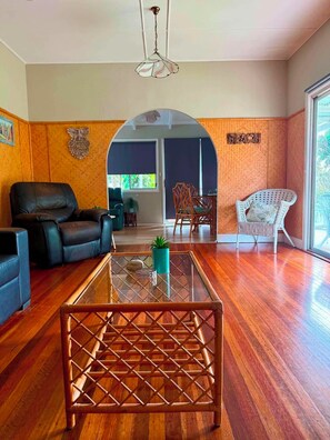 Amplia sala de estar con mesa de centro de vidrio, sofá de cuero, sillón de mimbre y vista a un balcón a través de un arco.