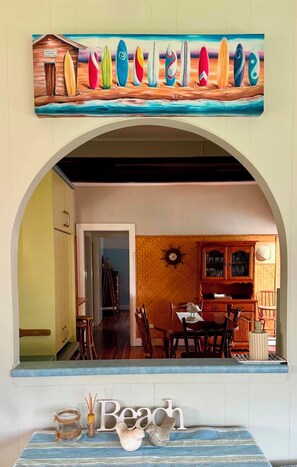 A beach-themed interior with a dining area, wooden cabinets, and a sign above the archway.