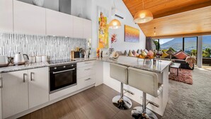 Una cocina moderna con armarios blancos, una isla central con taburetes y un amplio ventanal con vistas a la montaña.