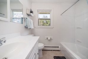 Une salle de bain avec une baignoire blanche, un lavabo blanc et des toilettes. Il y a une fenêtre au-dessus des toilettes et un porte-serviettes avec des serviettes.