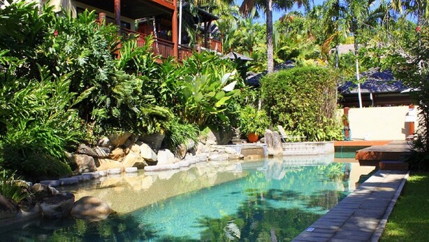 Una piscina cristalina rodeada de exuberante vegetación y un edificio con techo rojo.
