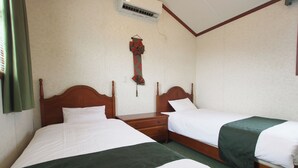 A hotel room with two single beds, a wooden nightstand, a green bedspread, and a wall-mounted air conditioning unit. - cottage NORTH OKINAWA (Nakijin)