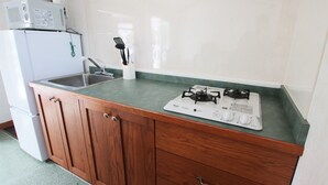 A compact kitchen with a sink, wooden cabinets, a microwave, and a gas stove. - cottage NORTH OKINAWA (Nakijin)