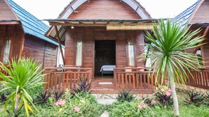 Una cabaña de madera con porche, rodeada de plantas tropicales.