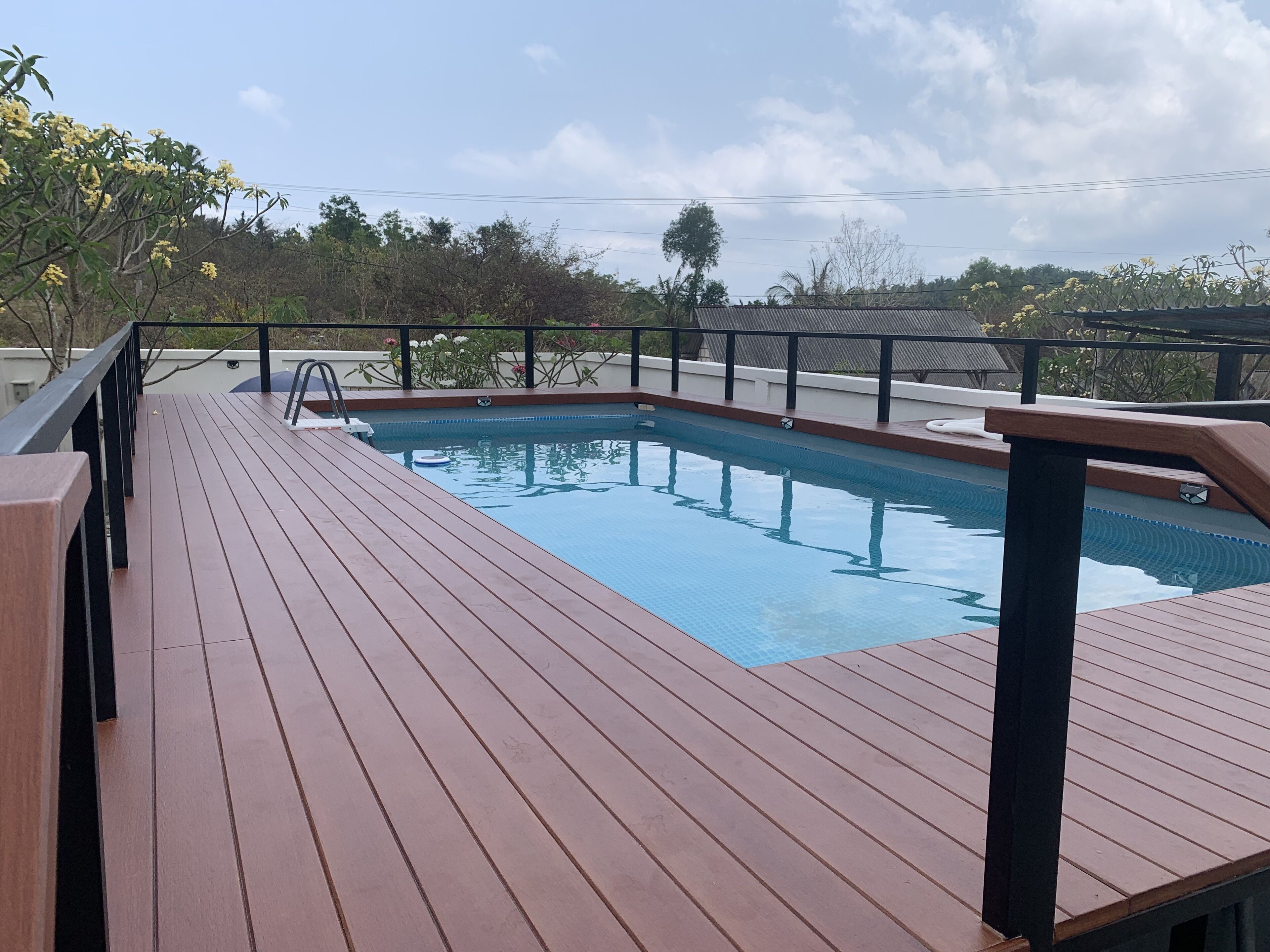 A wooden deck with a swimming pool, surrounded by a metal railing and trees.