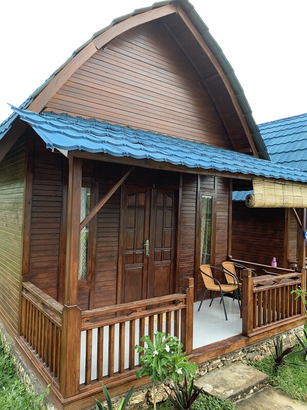 A wooden house with a porch, a number '4' on the door, and a blue roof. - Tanah Penida Bungalow (Penida Island)
