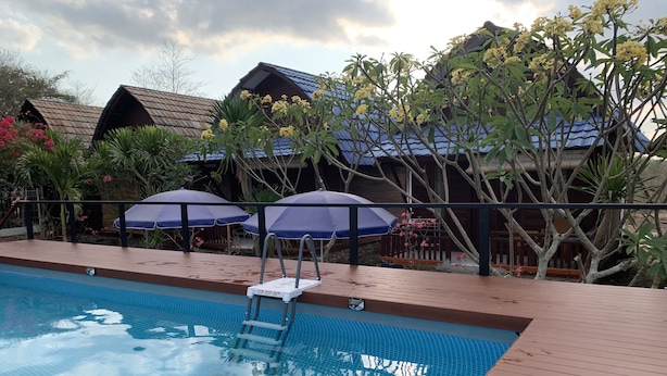 Una piscina con cubierta de madera, dos sombrillas y vista a edificios de madera al fondo.