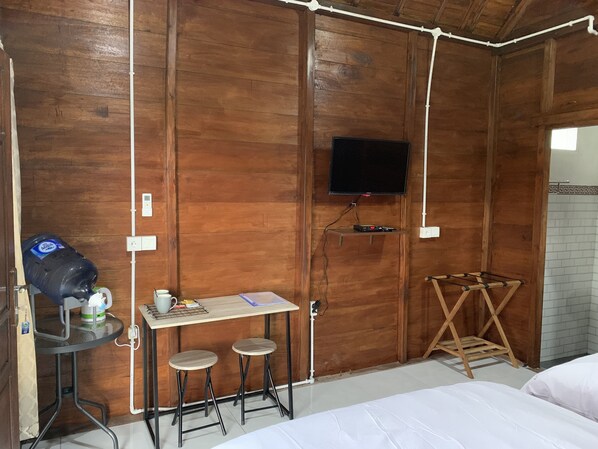 Una habitación de madera con una cama, una mesita con taburetes, un televisor en la pared y un dispensador de agua.