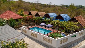 Un espace piscine agrémenté de plusieurs bungalows, chacun ayant une couleur de toit différente.