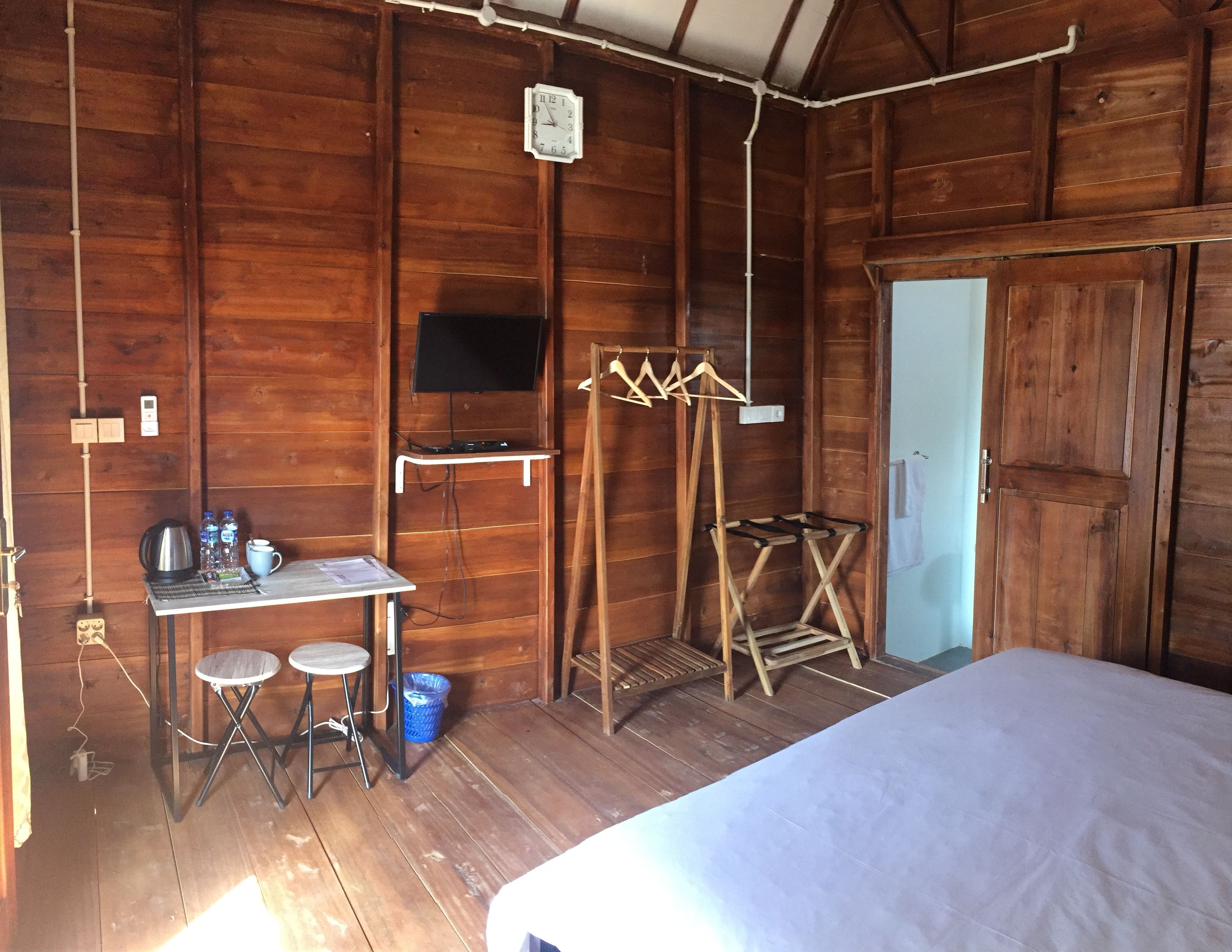 Una habitación de cabaña de madera con una cama, una mesita con una tetera, tazas y botellas, un televisor montado en la pared y un perchero de madera.