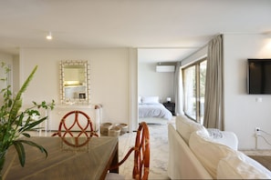 A hotel room with a bed, a sofa, a dining area with a table and chairs, a mirror, and a television. - Family friendly lux apartment by the beach w/ pool,best view, 25mins from Athen (Vouliagmeni, Athens)