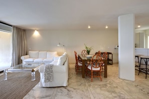 A modern living room with a white sofa, a glass coffee table, and a dining area with wooden chairs and a table. - Family friendly lux apartment by the beach w/ pool,best view, 25mins from Athen (Vouliagmeni, Athens)
