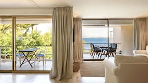 En rummelig opholdsstue med en stor skydedør, der fører til en balkon med bord og stole, med udsigt over et smukt havlandskab.