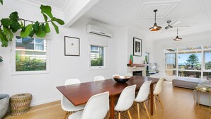 Uma sala de jantar moderna com uma mesa de madeira, cadeiras brancas e uma grande janela com vista para o exterior.
